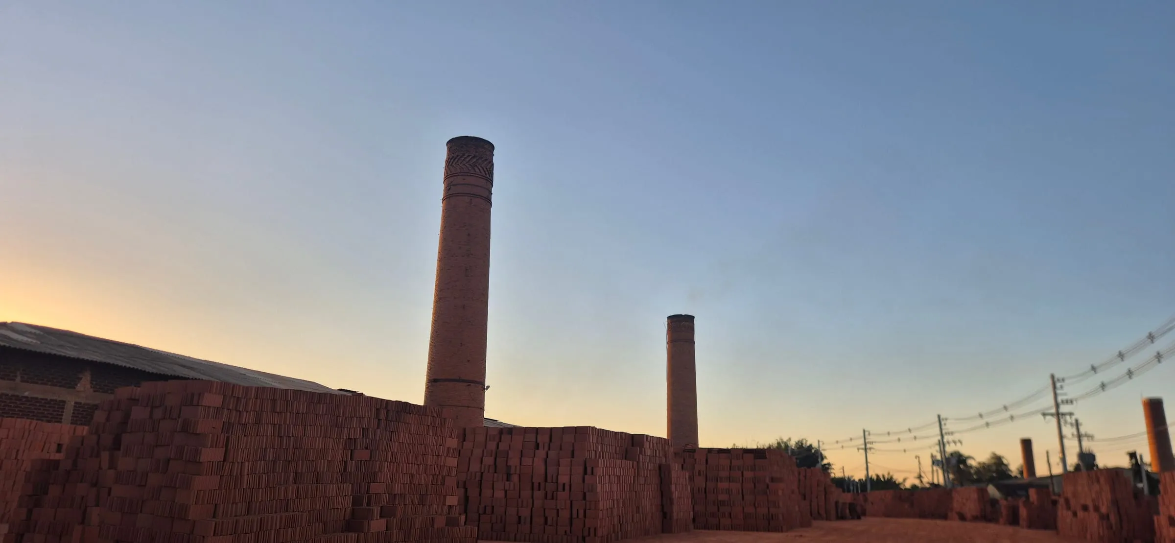 Chaminés da Cerâmica Argiplan ao entardecer, com pilhas de tijolos cerâmicos no pátio